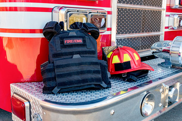 Ballistic vest and red firefighter helment on fire truck bumper. Concept of evolving role of fire...