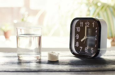 fish collagen powder and a glass of water near alarm clock. morning collagen peptides intake.