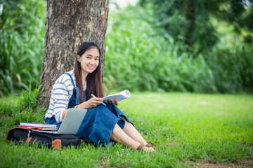 beautiful Asian girl student holding books and smiling at camera and learning and education concept  on park in summer for relax time