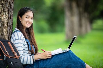 beautiful Asian girl student holding books and smiling at camera and learning and education concept  on park in summer for relax time