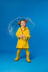 child girl blonde smiling in a yellow raincoat and rubber boots holding an umbrella stands on a...