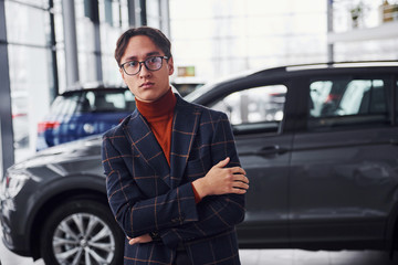 Fototapeta na wymiar Posing for the camera. Young business man in luxury suit and formal clothes is indoors near the car
