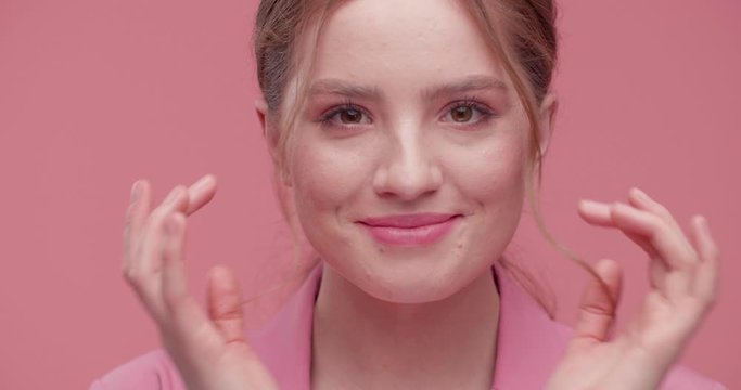 Young red-haired Woman with Wrinkles is touching her perfect Skin pleasurably. Extremely beautiful Girl is applying Cream on her healthy Skin, Beauty Concept. Pink Studio, nice Makeup. Beauty, Faces.