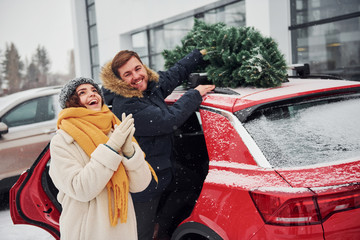 Young couple standing near car with tree on the top. Together outdoors at winter time