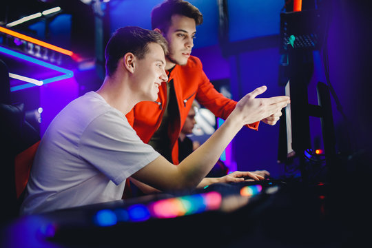 Team Of Two Guys Playing Online Video Games Analyzes Strategy Of Fighting Behind Computer Monitor In Internet Cafe