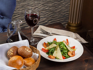 Arugula salad with shrimps, slices of parmesan, fresh tomatoes and pesto in a plate on a restaurant table