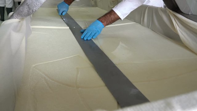 Man's Hand With Knife Cutting A Cheese on the Cheese Production Line