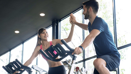 Sporty woman and man giving each other a high five after cycling training in gym. 