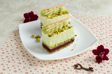 Contemporary cherry and pistachio mousse cakes decorated with red flowers on white plate on light background