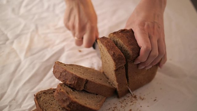 Woman cuting rye bread by huge knife on the white table