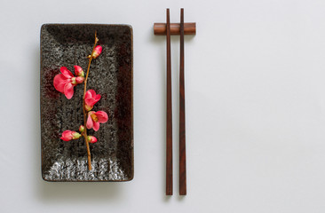 Chopsticks, rectangular plate and pink flowers on gray background