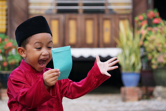A Malay boy in Malay traditional cloth showing his happy reaction after receiving money pocket or 'Duit Raya' during Eid Fitri or Hari Raya celebration.