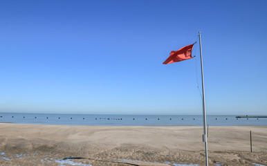 red flag blowing on empty beach in the winter