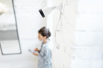 Woman controls home video surveillance with a smartphone indoors, view from the above and ip camera on the foreground. Concept of a wireless home security systems