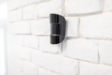 Black wireless motion sensor of alarm system mounted on the white brick wall indoors