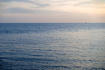 View of a small sailboat on the open sea horizon.