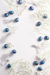 Easter farme with quail eggs painted blue, feathers and gypsophila flowers flat lay, hard light, harsch shadows, copy space.