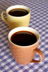 Vertical Image of Two Cups of Hot Black Coffee on Purple Check Pattern Tablecloth