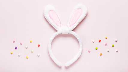 Funny cute bunny eggs and bunny rabbit ears for kids on pastel pink table top, Easter holiday concept. Easter decoration for kids flat lay, copy space