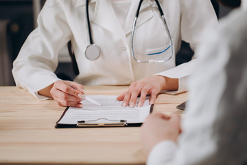Cropped photo of female physician interviewing a patient and filling in medical documents