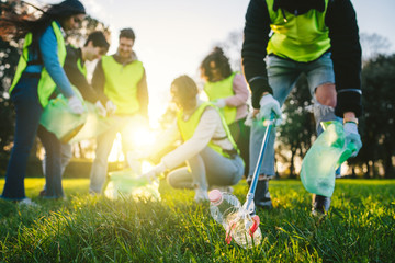 Group of friends during a volunteer garbage collection event in a park at sunset - Millennial having fun together - Happy people cleaning area with bags - Ecology concept - 330142635