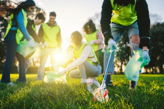 Group of friends during a volunteer garbage collection event in a park at sunset - Millennial having fun together - Happy people cleaning area with bags - Ecology concept