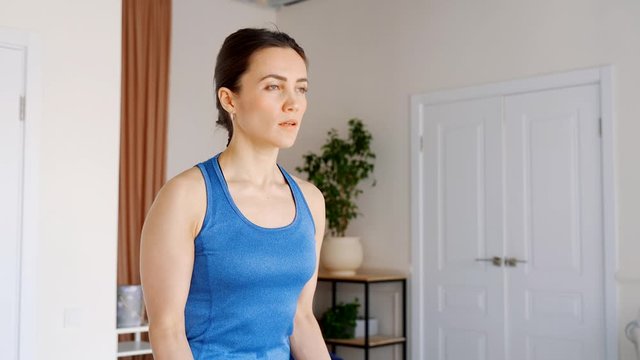 Strong beautiful girl in sportswear doing biceps exercise using a rubber expander.She is Training at Home in Her Living Room with Cozy Interior.