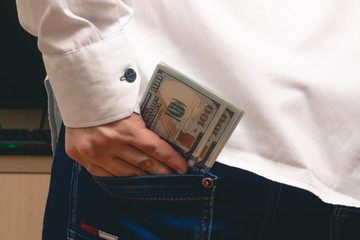 a man puts in his back pocket jeans a pack of hundred-dollar bills in a white shirt in the office