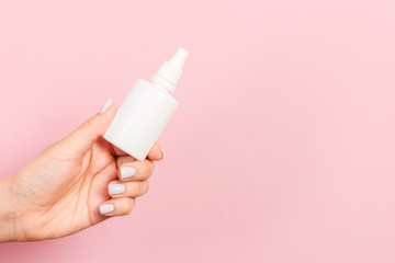 A bottle of nasal spray in a female hand at pink background with empty space for your design - obrazy, fototapety, plakaty