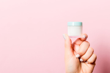 Female hand holding cosmetics jar at pink background with empty space for your design
