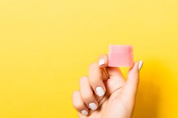Close up of cosmetics jar in female hand at yellow background with copy space