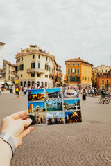 The guy is holding a card of Verona with many attractions on cityscape background.