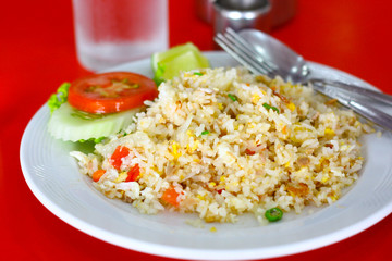 Fried rice on white round plate set on red table with fork, spoon and glass of water.