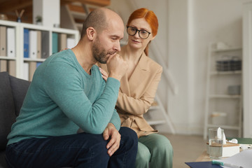 Young psychologist sitting on the sofa together with her patient and trying to calm him and support during therapy at the office