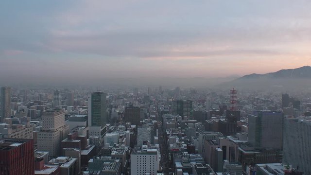 SAPPORO, HOKKAIDO, JAPAN - FEB 2020 : Aerial high angle sunset view of cityscape of Sapporo city. View of buildings and street traffic around Susukino downtown area. Time lapse shot sunset to night.