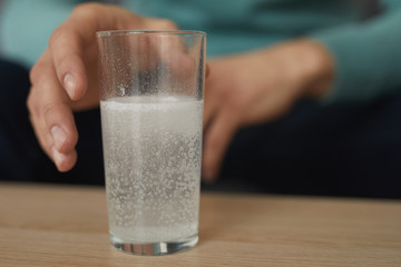 Close-up of glass with painkiller on the table and man holding out his hand for it in the background