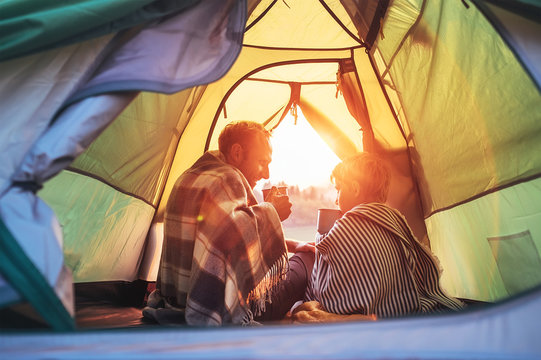 Father And Son Drink Hot Tea Sitting Together In Camping Tent. Traveling With Kids And Active People Concept Image.