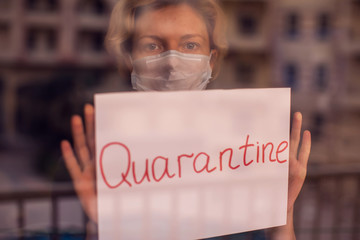 A portrait of woman indoor behind the window holding paper with word Quarantine. People, medicine,...