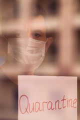 A portrait of man indoor behind the window holding paper with word Quarantine. People, medicine,...