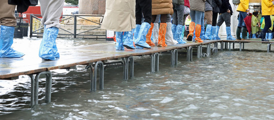 People walking with plastic gaiters during high tide in Venice