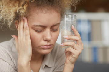 Close-up of woman holding glass with painkiller and drinking it from headache