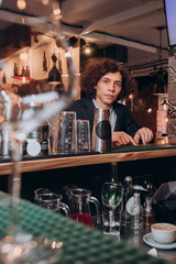 young curly haired guy in a black suit is sitting on a chair in a bar
