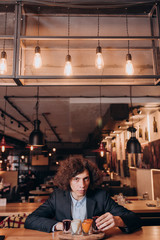 young curly-haired guy in a black suit drinking a liqueur in the bar