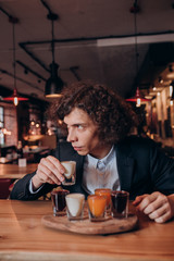 young curly-haired guy in a black suit drinking a liqueur in the bar