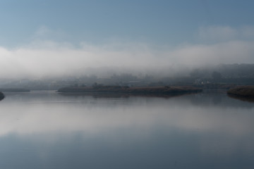 Fototapeta na wymiar Fog river landscape at sunrise with low clouds and reflection on the water in Alcacer do Sal, Portugal