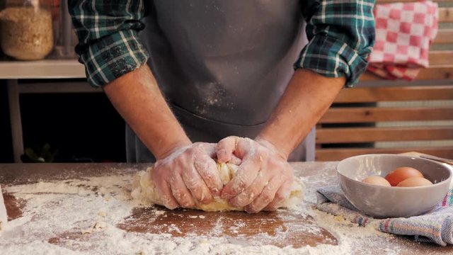 Male hands clapping and sprinkling white flour over dough on kitchen