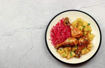 Baked chicken with potatoes served with cabbage salad in a plate on a light background. Top view, flat lay