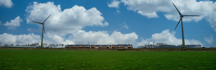 Panoramic dutch landscape with passenger train and two wind turbines