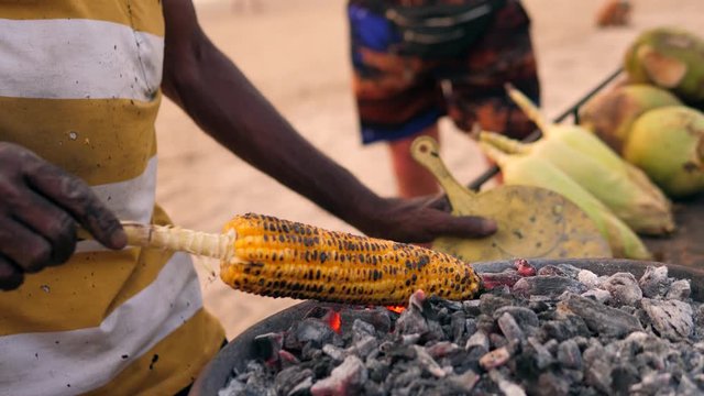 Corn cobs on the grill. Close-up image with corns and hands. Asian, Indian and Chinese street food. Trolley on the beach GOA
