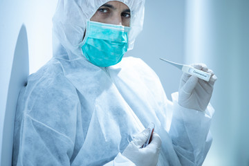 medico con tuta protettiva e mascherina tiene in mano untermometro  per con su scritto l...